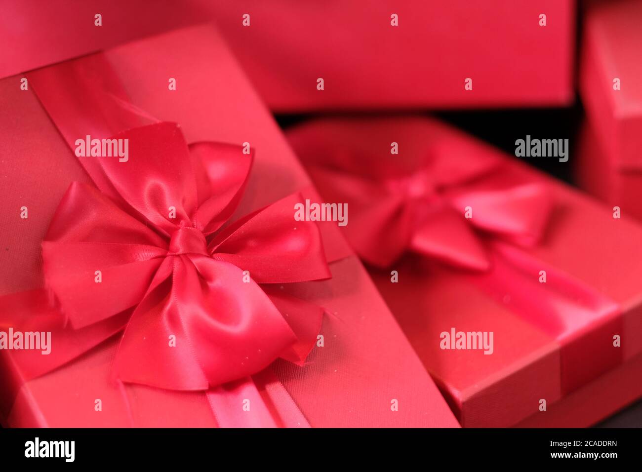 primo piano con un mucchio di confezioni regalo rosso brillante con arco a nastro. Sfocatura dello sfondo Foto Stock