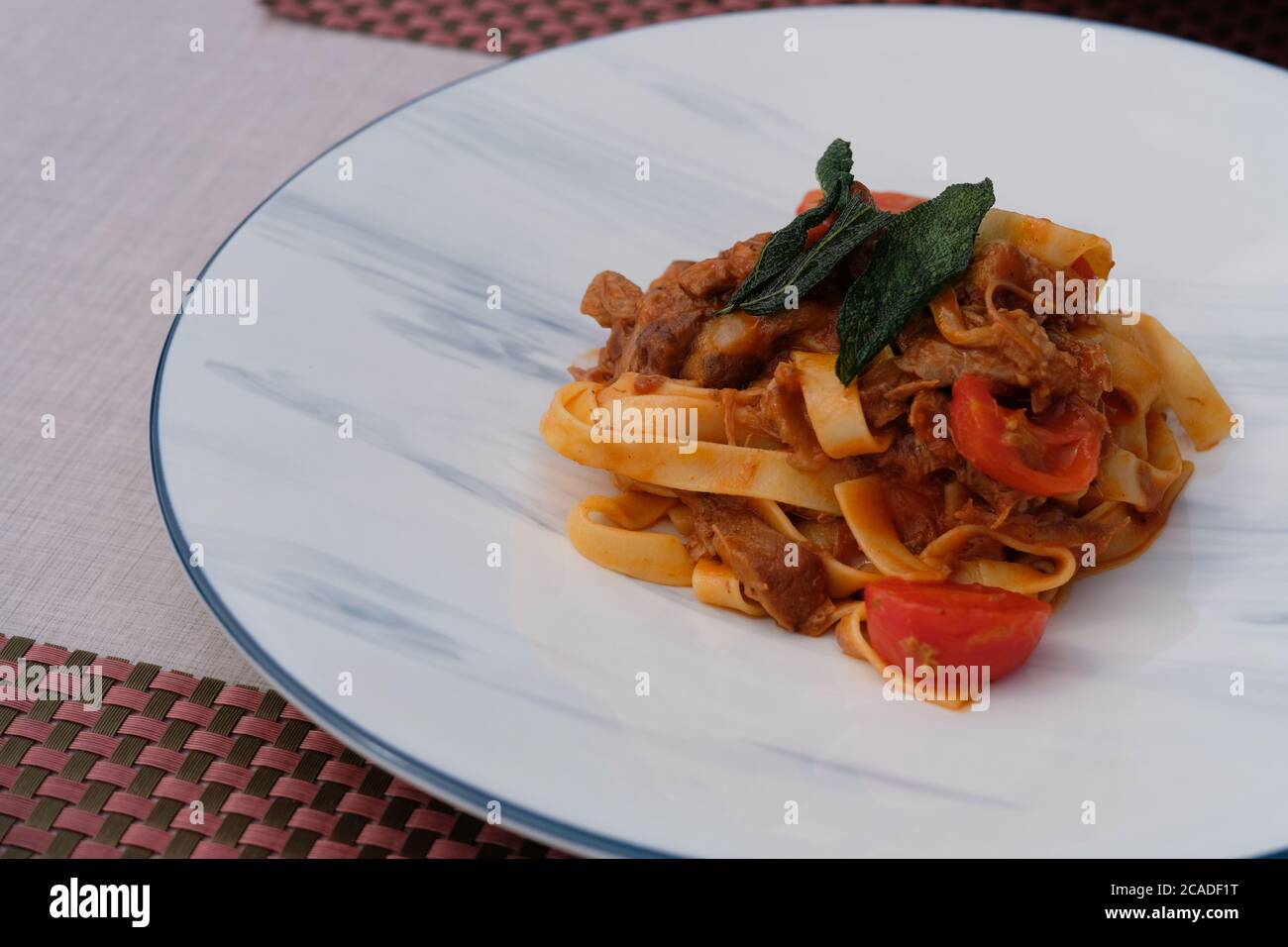 primo piano fettuccine con carne e pomodoro in piatto a motivi bianchi. Noodle italiano. Sfocatura dello sfondo Foto Stock