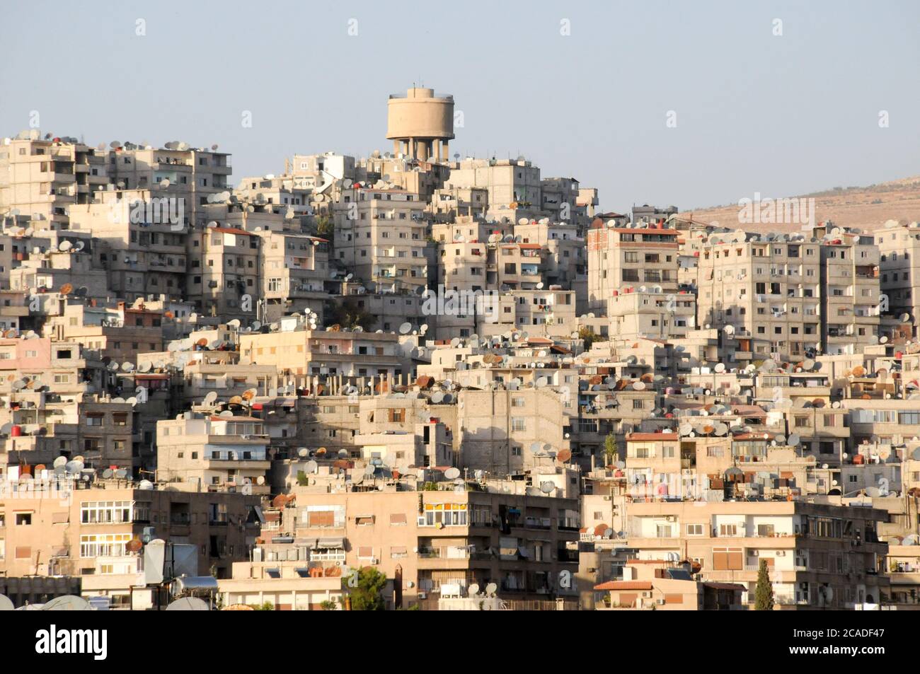 Un gruppo densamente popolato di bassi blocchi di appartamenti e una torre d'acqua nel quartiere residenziale suburbano di Mezzeh, a Damasco, Siria. Foto Stock