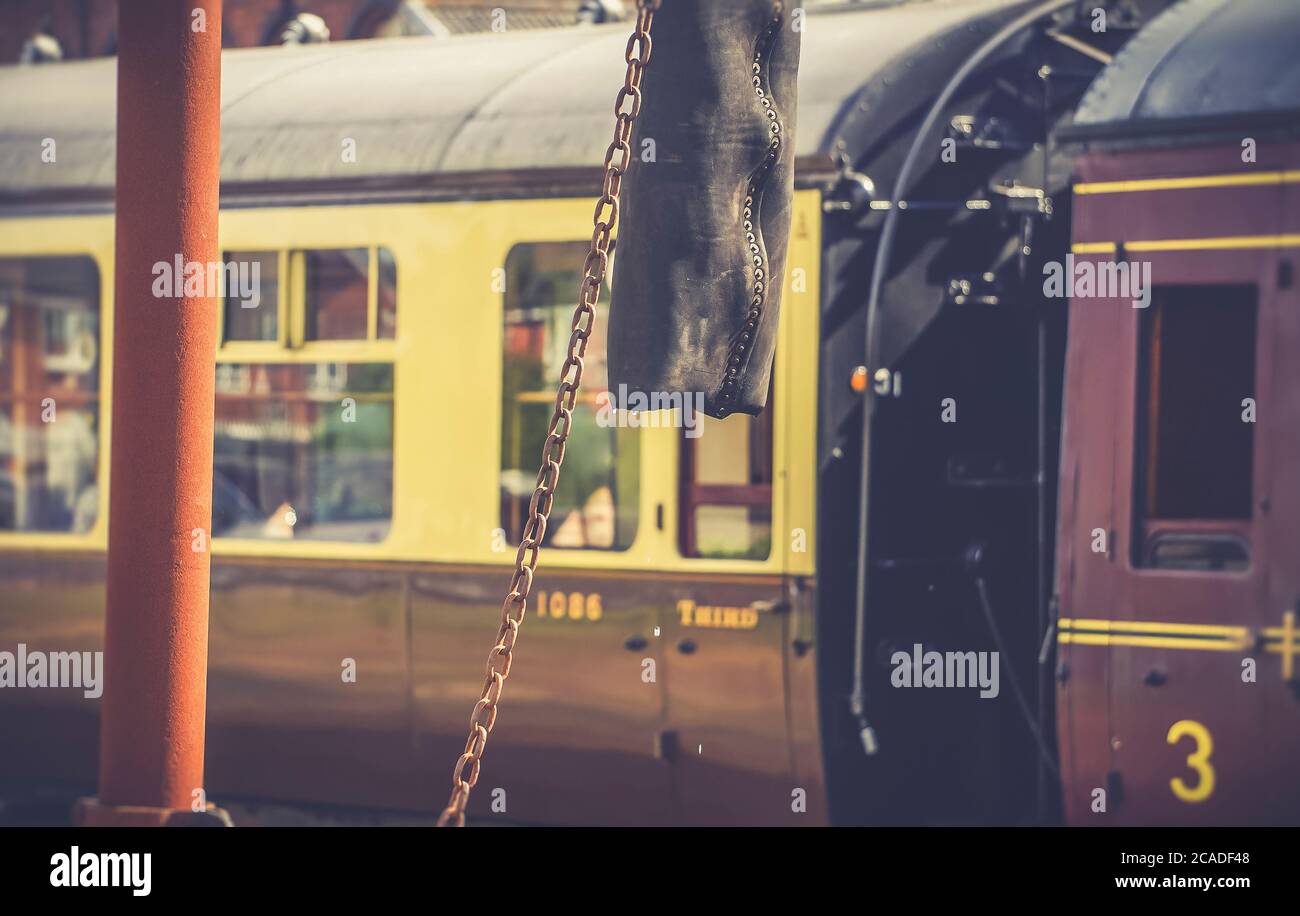 Primo piano della gru d'acqua d'epoca nei pressi della stazione ferroviaria del patrimonio britannico dopo aver riempito il serbatoio del motore a vapore. Carrozza vintage di treno a vapore dietro. Foto Stock