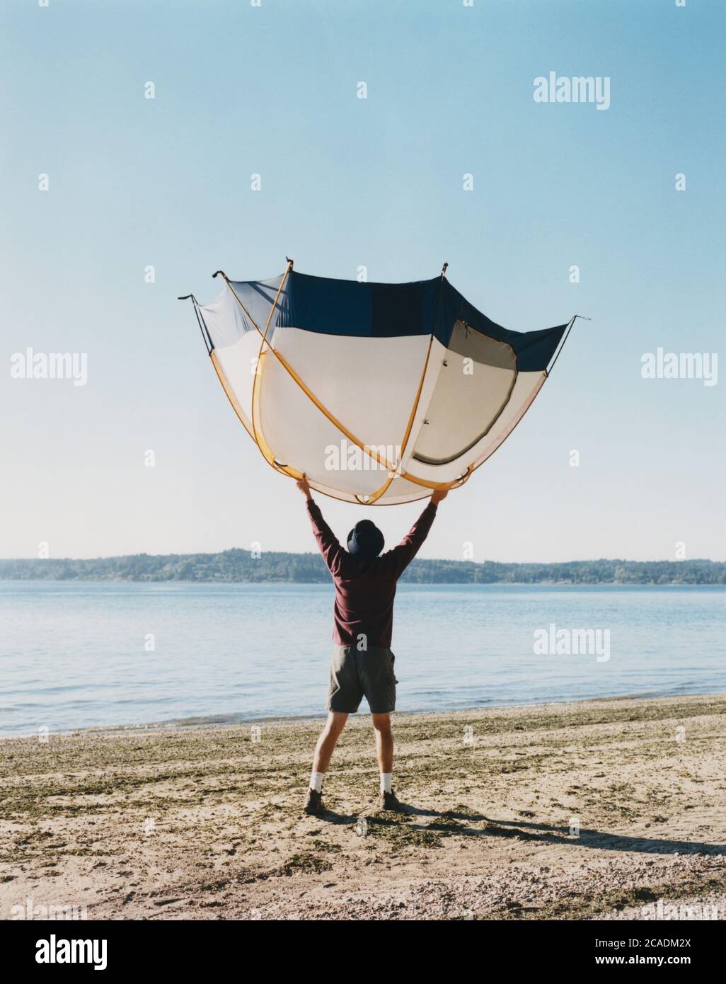 Un uomo che tiene una piccola tenda a cupola sopra la testa, in piedi sulla spiaggia Foto Stock