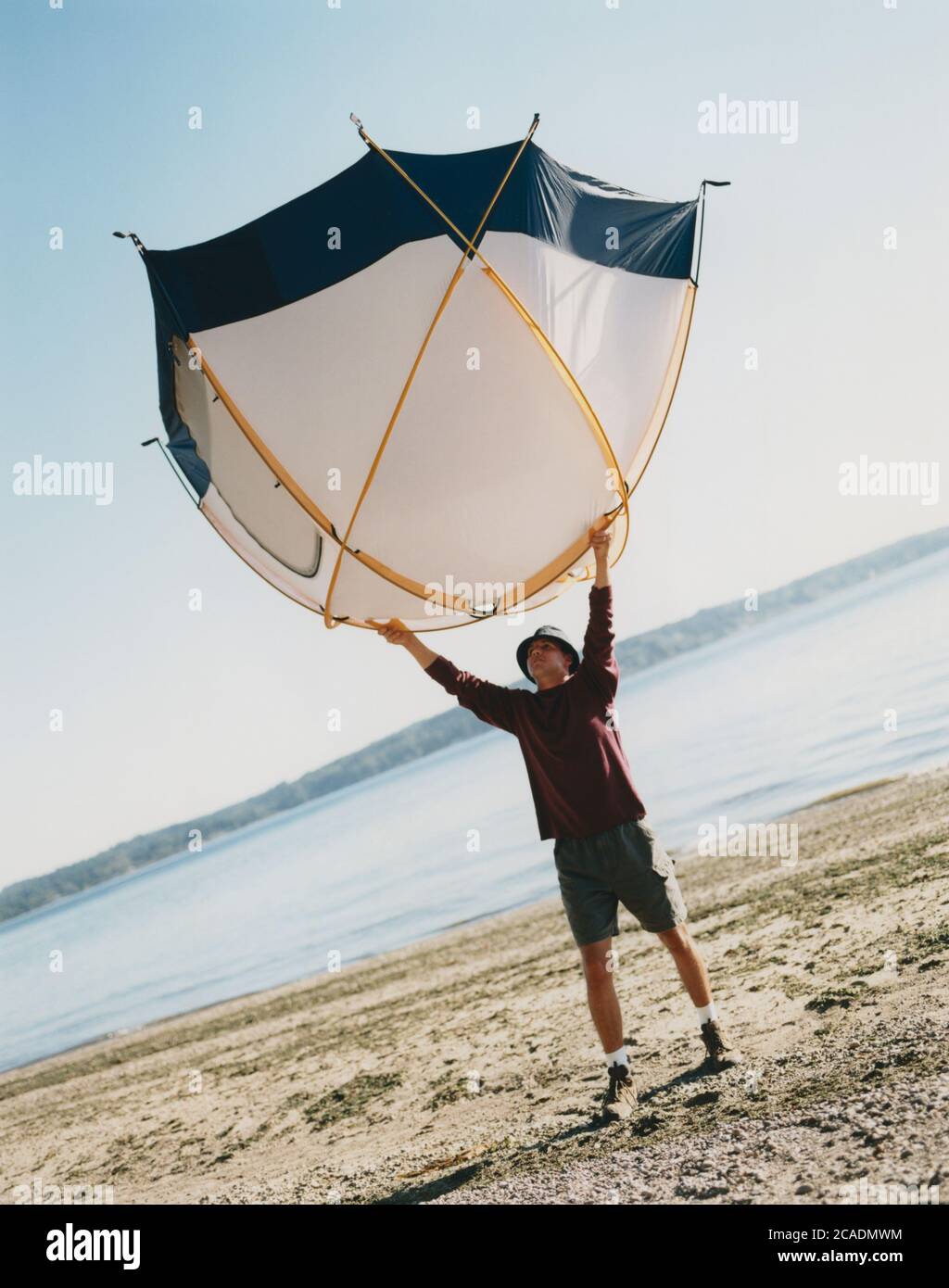 Un uomo che tiene una piccola tenda a cupola sopra la testa, in piedi sulla spiaggia Foto Stock