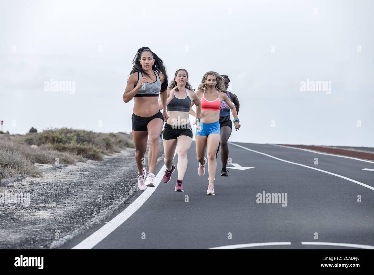 Corpo pieno le donne sportive forti che corrono una dopo l'altra verso la fotocamera durante l'allenamento all'aperto in giornata grigia in periferia Foto Stock
