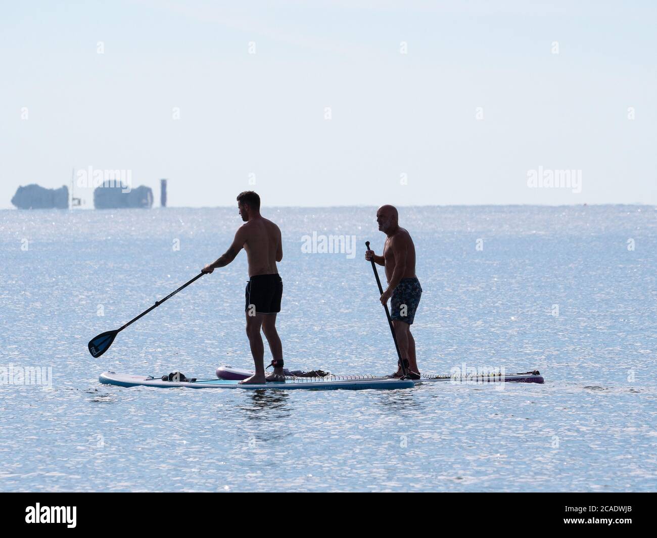 2 uomini su tavole da paddleboard al largo della costa di Mudeford vicino Christchurch, Dorset, con gli aghi sull'isola di Wight alle spalle. Foto Stock