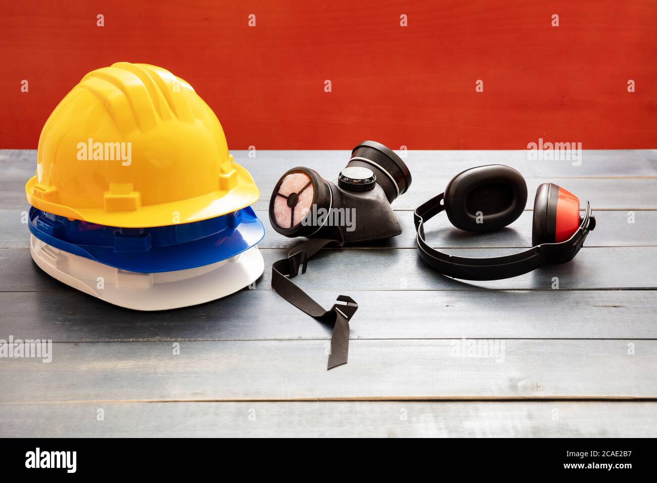 Attrezzatura di protezione per la sicurezza sul lavoro. Dispositivi di protezione industriale su tavolo in legno, sfondo rosso. Concetto di salute e sicurezza del cantiere Foto Stock