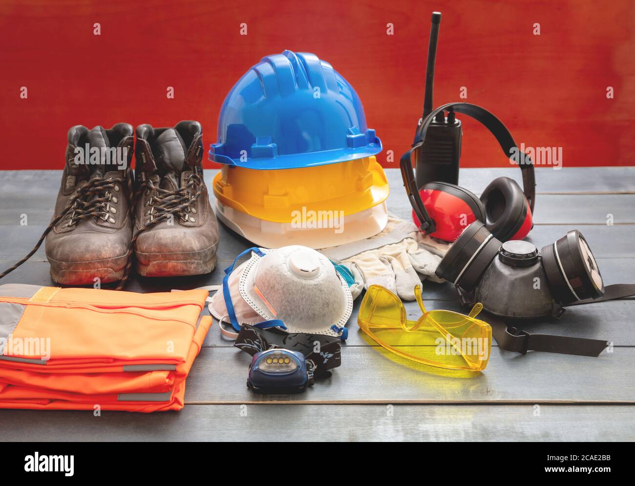 Attrezzatura di protezione per la sicurezza sul lavoro. Dispositivi di protezione industriale su tavolo in legno, sfondo rosso. Concetto di salute e sicurezza del cantiere Foto Stock