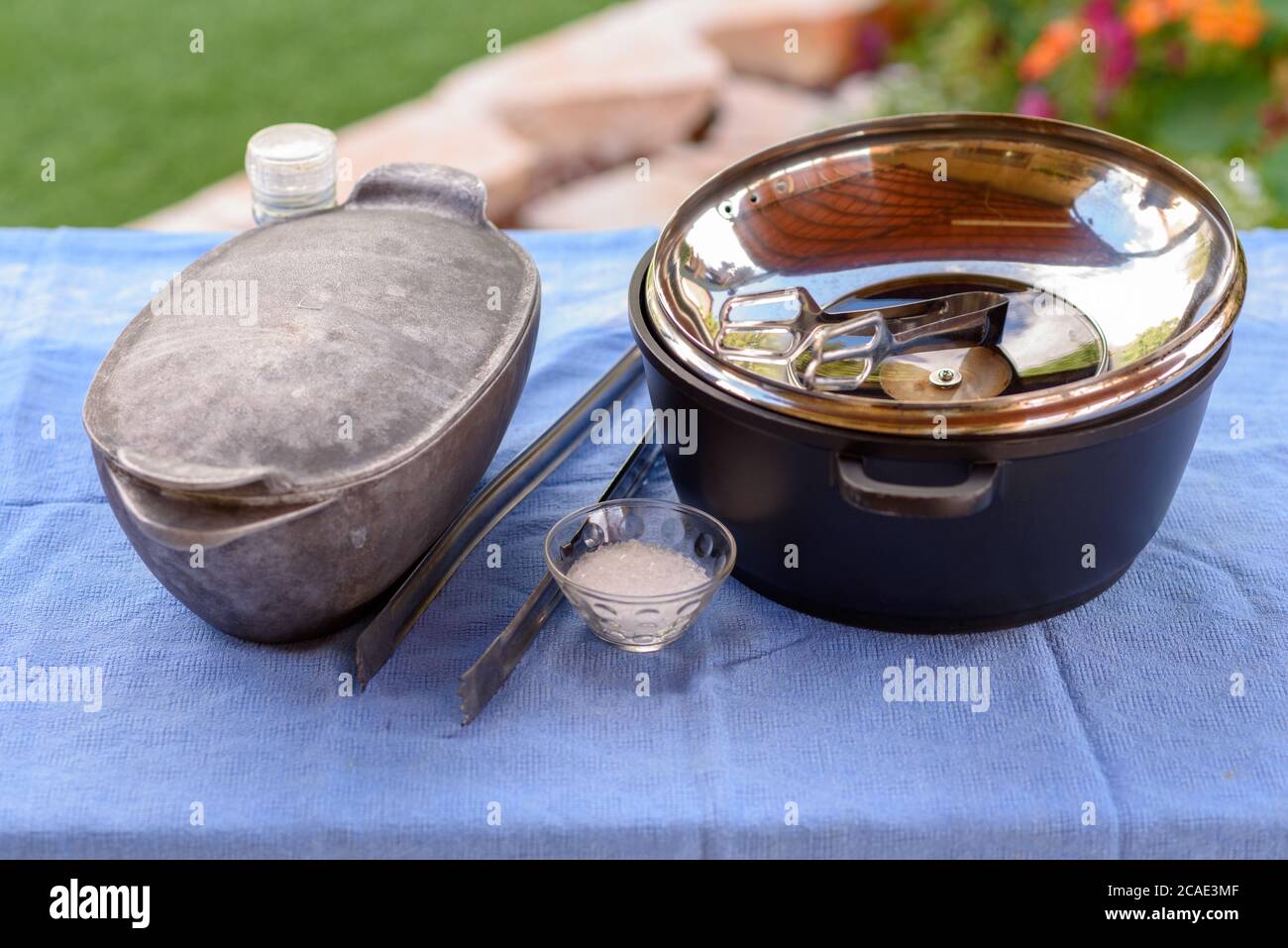 Preparandosi per un barbecue all'aperto nel Giardino d'Estate. Pentole, pinze per barbecue, sale, spezie su un tavolo con una tovaglia blu. Stile retro. Foto Stock