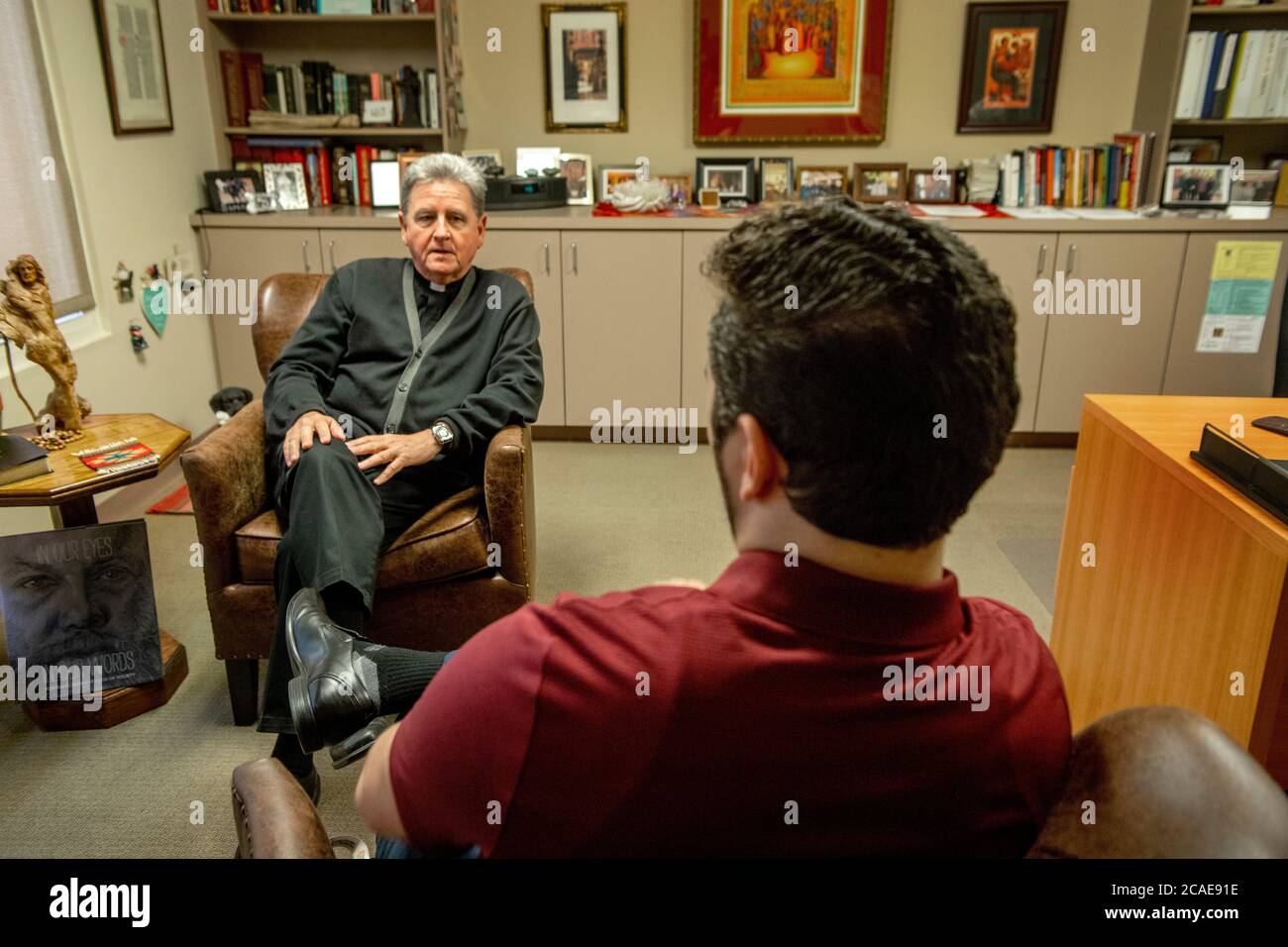 Nel suo ufficio presso una chiesa cattolica della California meridionale, un monsignor di mezza età consiglia un giovane parishioner adulto maschio. Foto Stock