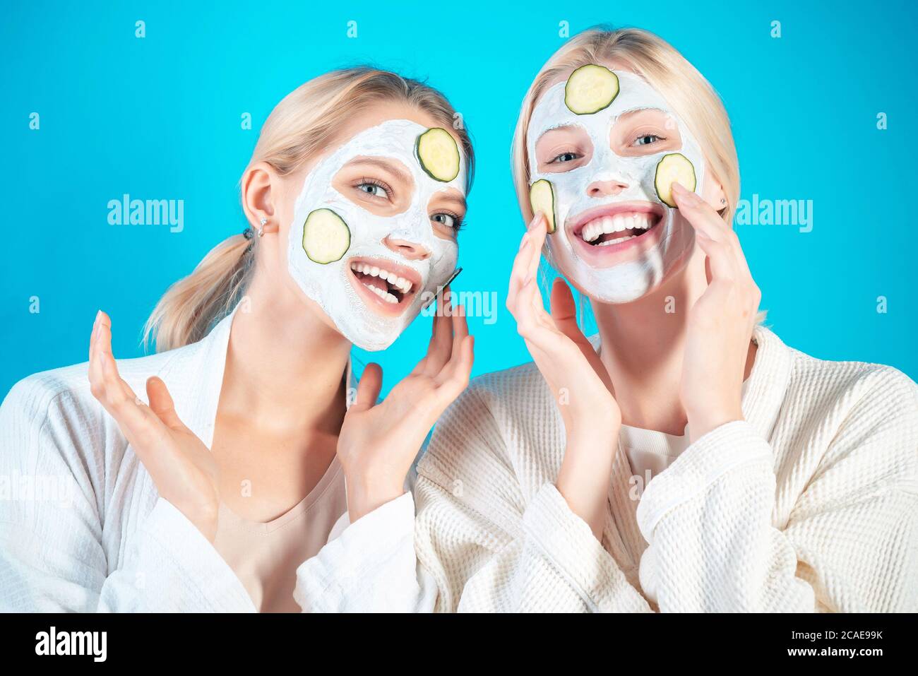 Le ragazze felici giovani fanno la maschera facciale con le fette di cetriolo a sfondo blu. Cura e trattamento della pelle, spa, bellezza naturale e concetto di cosmetologia. Foto Stock