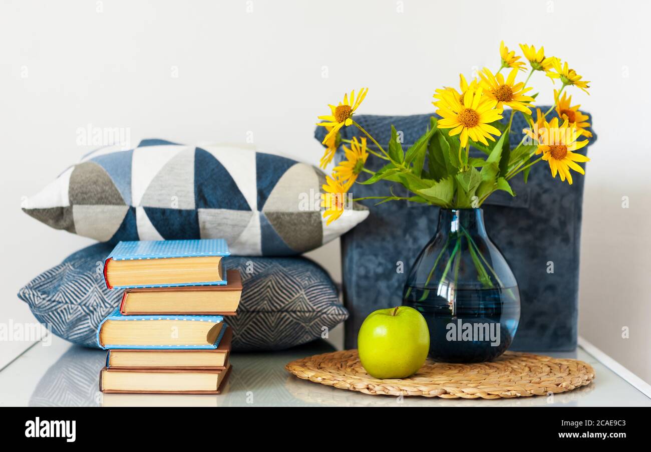 Arredamento interno accogliente: Pila di libri, mela verde, cuscini  decorativi, scatola con plaid e vaso con fiori gialli su un tavolo di  vetro. Distanza a casa Foto stock - Alamy