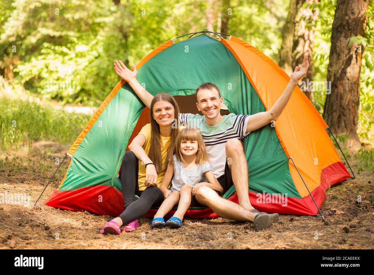 Ritratto all'aperto di una famiglia giovane e felice che gode della natura seduto vicino alla tenda del campeggio nella foresta estiva Foto Stock