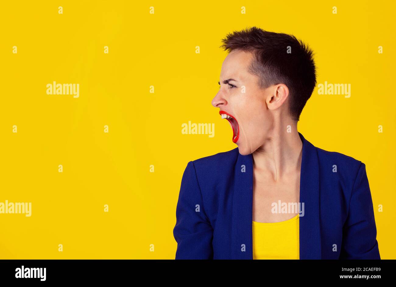 Rabbia. Closeup ritratto di donna arrabbiata in rabbia profilo laterale vista urlando bocca urlante aperta isolato su sfondo giallo. Modello in camicia gialla Foto Stock