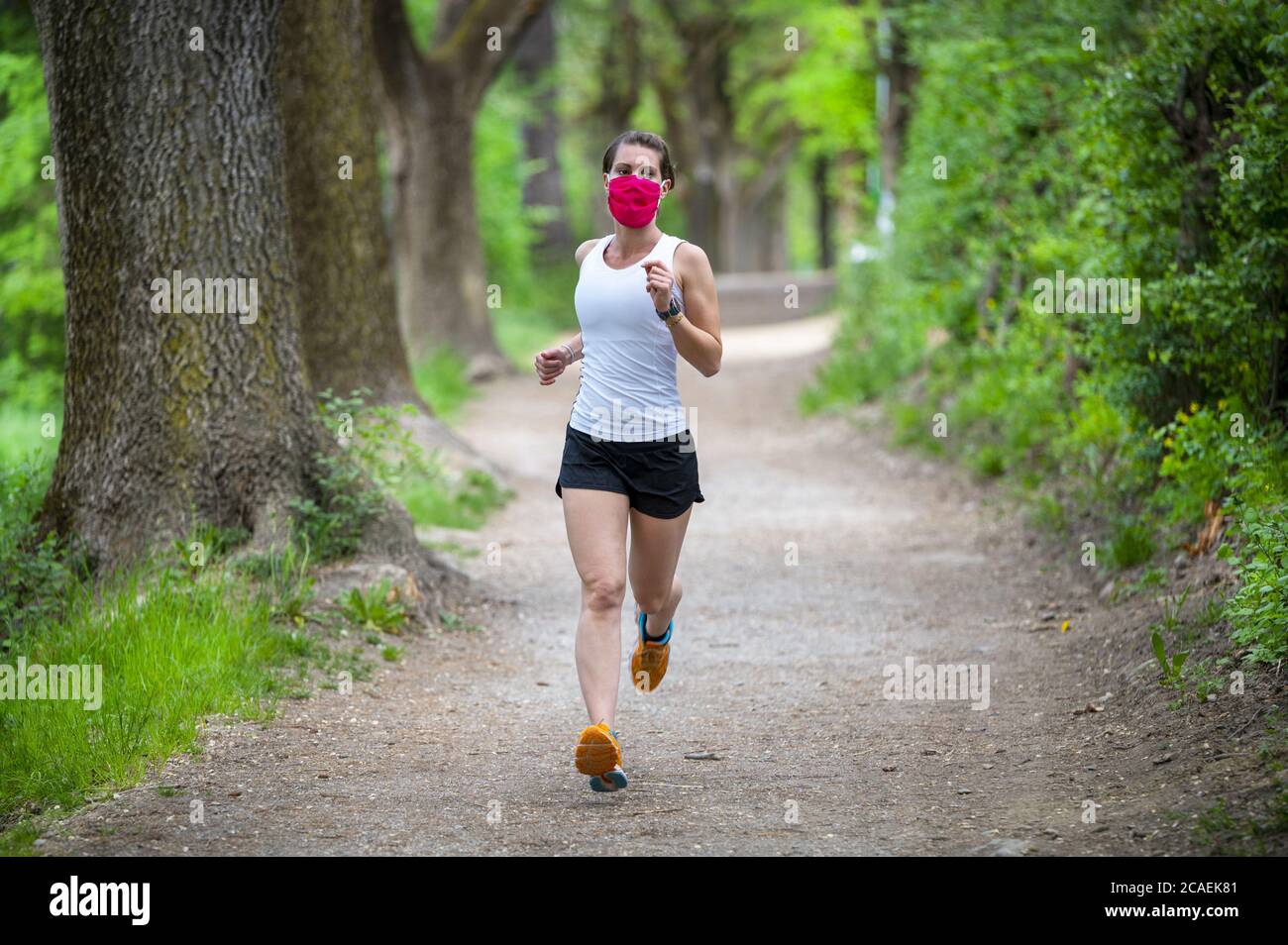 Mantenersi in forma durante il Coronavirus. Una donna sportiva sta facendo jogging all'aperto, ha una maschera protettiva sul viso. In esecuzione nei giorni del Covid-19. Foto Stock