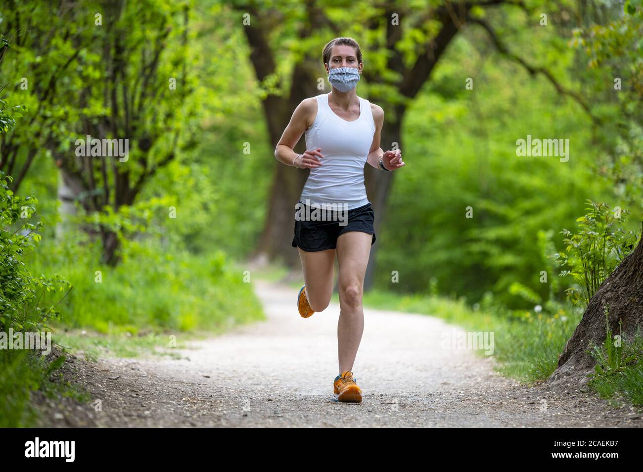 Mantenersi in forma durante il Coronavirus. Una donna sportiva sta facendo jogging all'aperto, ha una maschera protettiva sul viso. In esecuzione nei giorni del Covid-19. Foto Stock