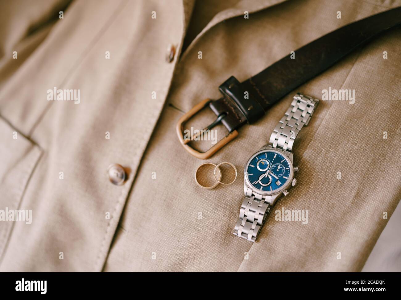 Cintura da uomo, orologio da polso e anelli da sposa su una giacca beige da uomo. Foto Stock
