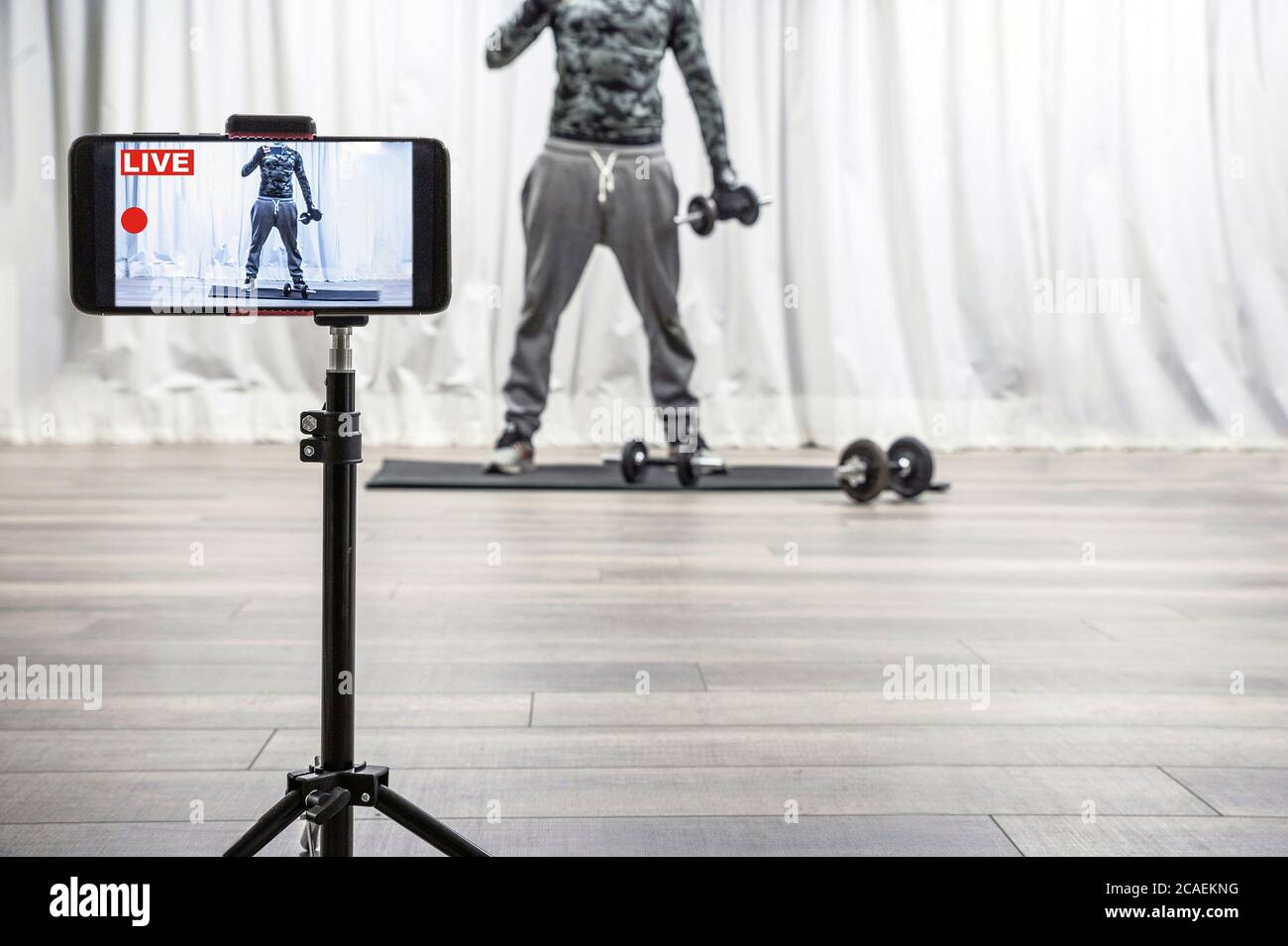 Uomo con gym dumbbell ed equilibrio. Esercizi di allenamento dal vivo su smartphone per seguaci sportivi sui social media. Coronavirus o quarantena Covid-19. Foto Stock