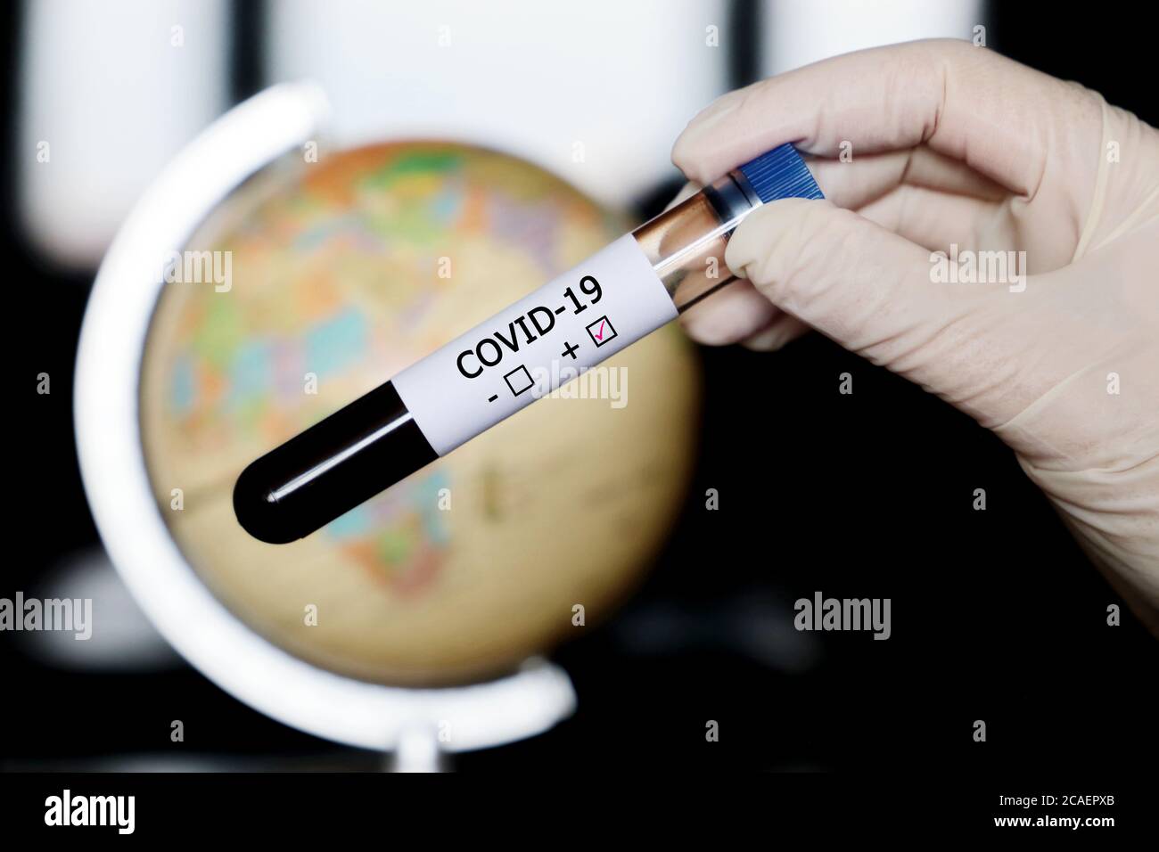 Provetta per analisi con campione di sangue covid-19 in mani sullo sfondo del globo. Medico con test positivo del coronavirus contro la mappa di Europa, Africa e Asia Foto Stock