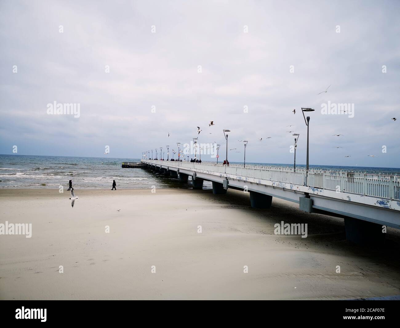 Una grande passerella uscendo verso il mare su un giorno nuvoloso con poche persone Foto Stock