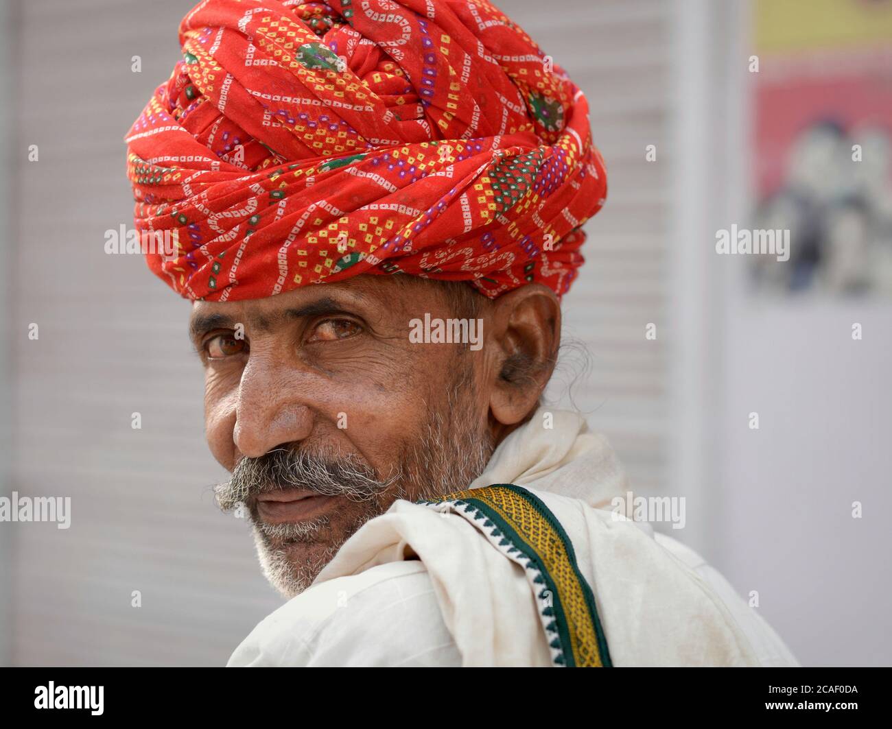 L'anziano Rajasthani indiano con il turbante rosso guarda indietro sopra la sua spalla. Foto Stock