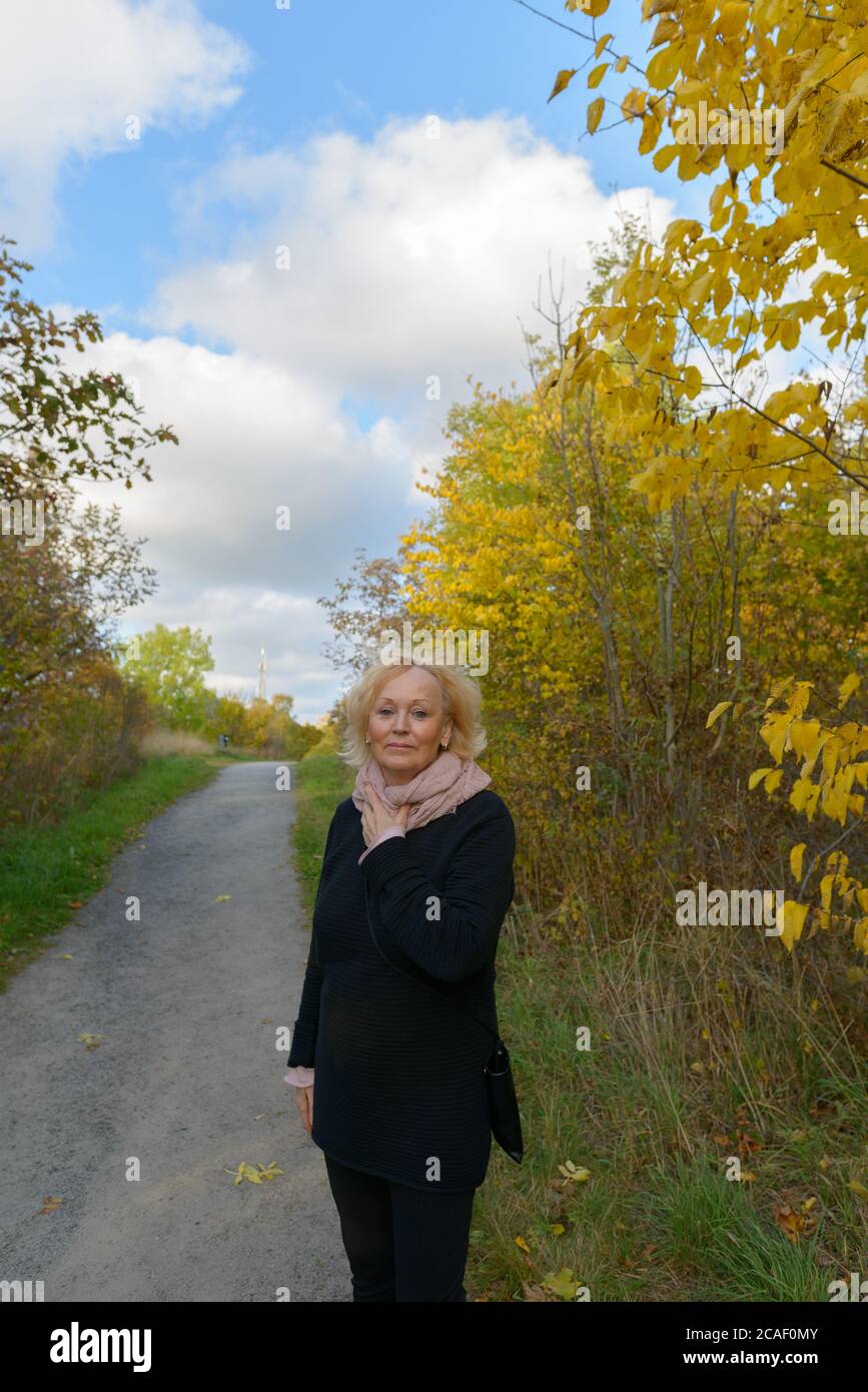 Donna anziana che tiene la sciarpa sul percorso con i giovani alberi d'autunno nel parco Foto Stock