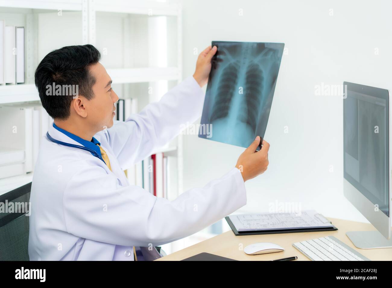 Medico asiatico che tiene e guarda all'esame dei raggi X dei polmoni e del cervello del paziente in una clinica medica in ospedale. Foto Stock