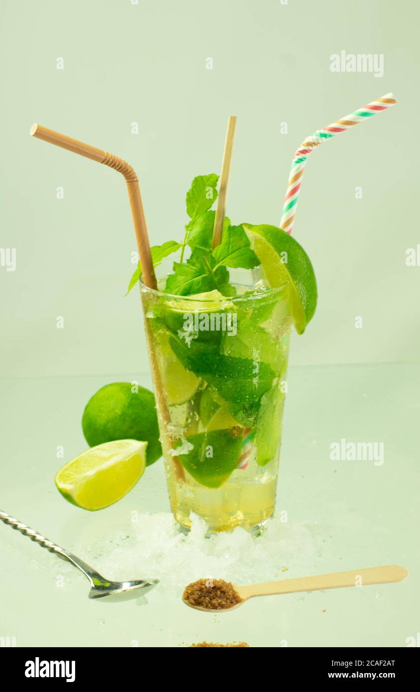 Colpo verticale di un cocktail mojito con foglie di rum, lime e menta su una superficie verde chiaro Foto Stock