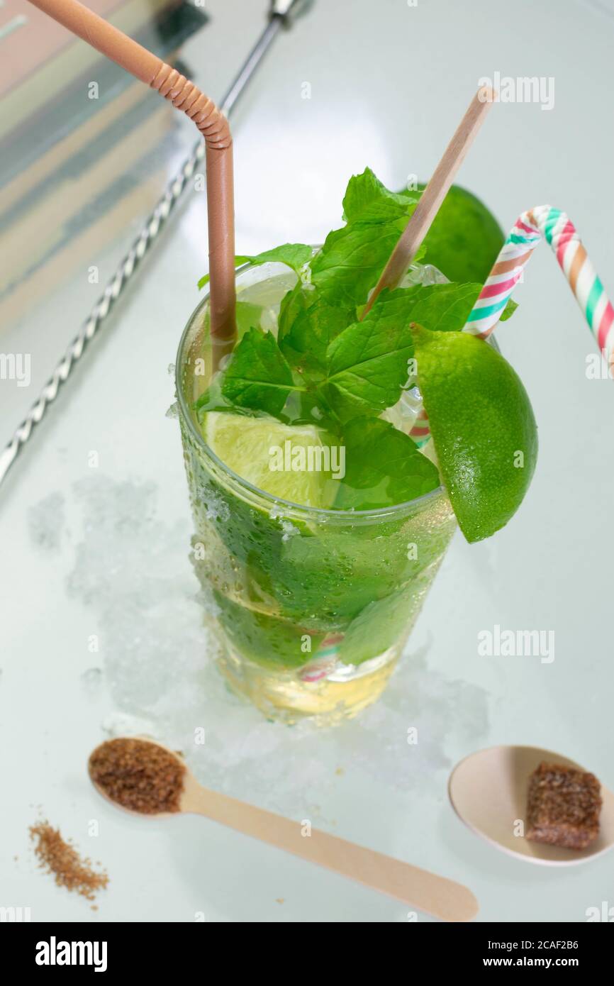 Colpo verticale di un cocktail mojito con foglie di rum, lime e menta su un tavolo di vetro Foto Stock