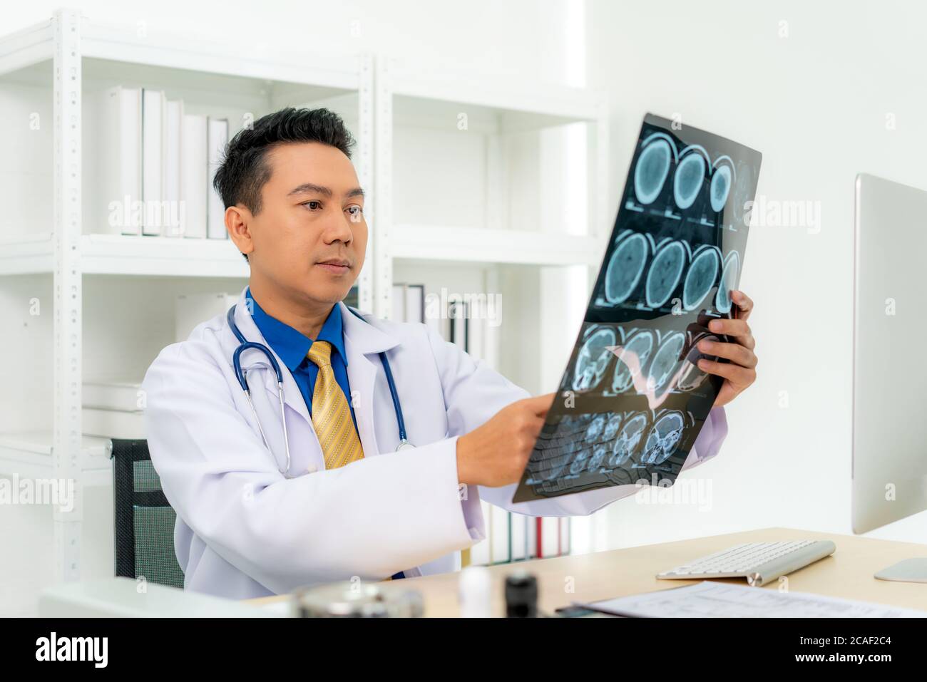 Medico asiatico che tiene e guarda all'esame radiografico del cranio e del cervello del paziente in una clinica medica in ospedale. Foto Stock