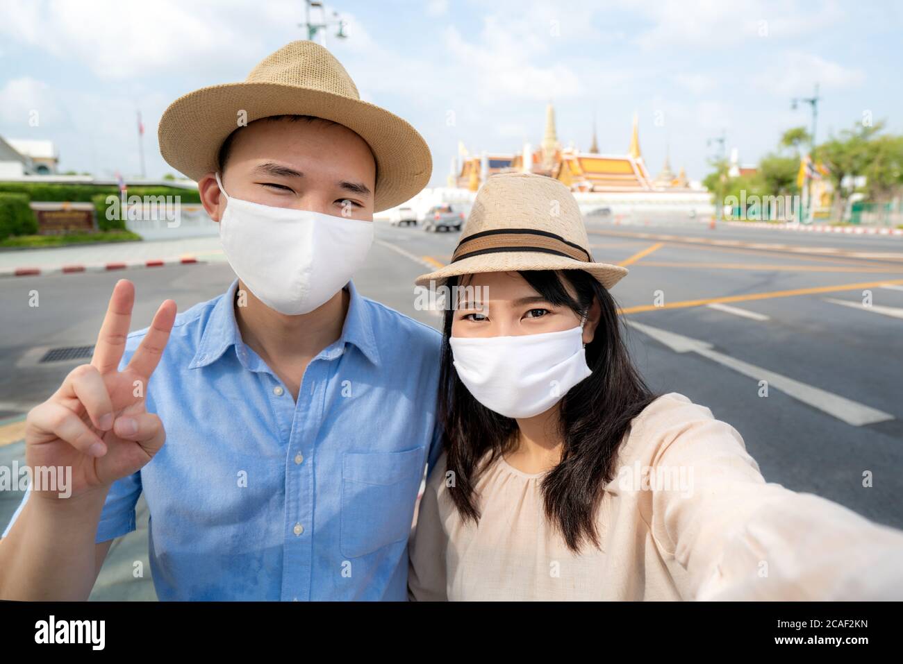 Coppia asiatica turisti felici di viaggiare indossando maschera per proteggere da Covid-19 in vacanza e selfie da fotocamera in Wat Phra Kaew Tempio a Bangkok, Foto Stock