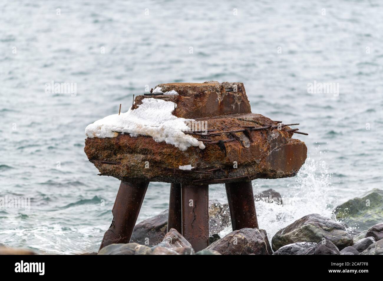 Un vecchio bacino vicino al bordo dell'oceano. Il molo di sterzo arrugginito è parzialmente sommerso in acqua e la parte in piedi ha neve su di esso. Foto Stock