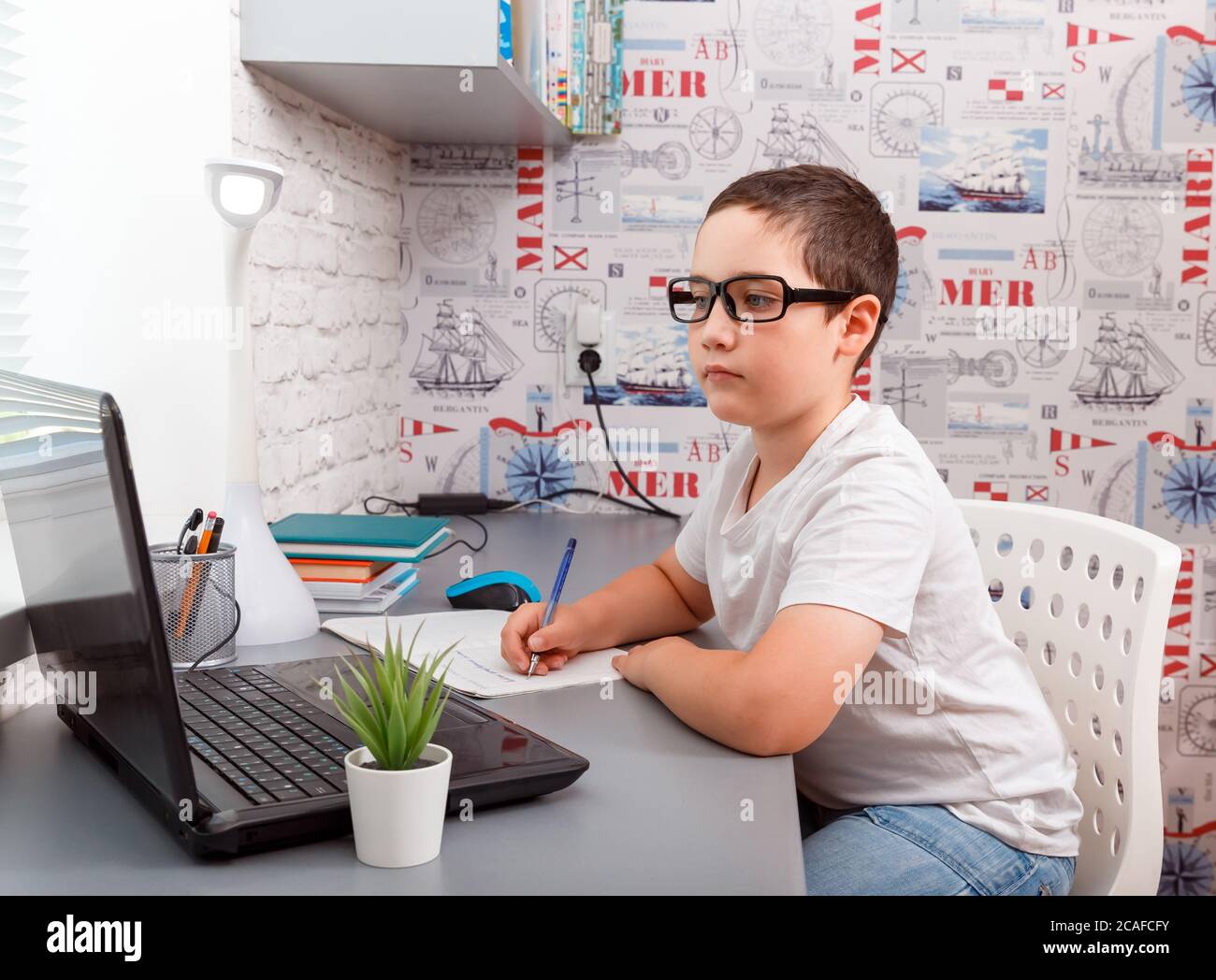 Bambino che usa il computer portatile mentre si siede alla scrivania con libro e si fa il lavoro Foto Stock