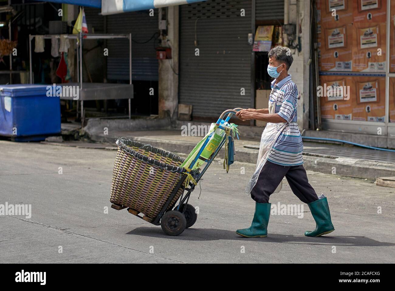 Thailandia scena di strada con l'uomo che indossa una maschera Covid-19 e utilizzando un carrello a mano per raccogliere merci di mercato. Thailandia, S. E. Asia Foto Stock