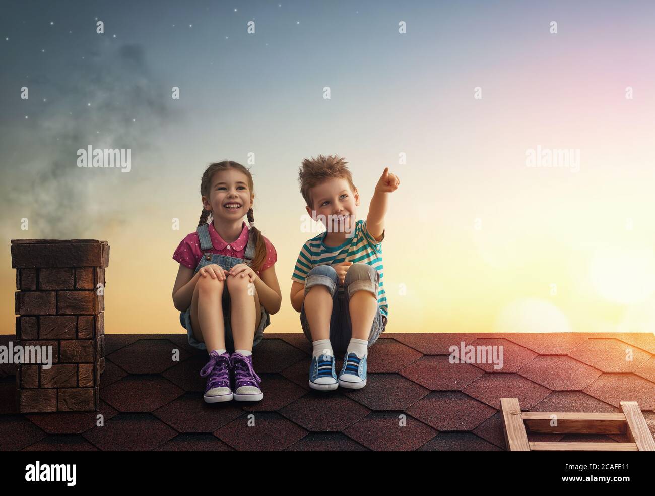 Due simpatici bambini si siedono sul tetto e guardano le stelle. Ragazzo e ragazza fanno un desiderio vedendo una stella di tiro. Foto Stock