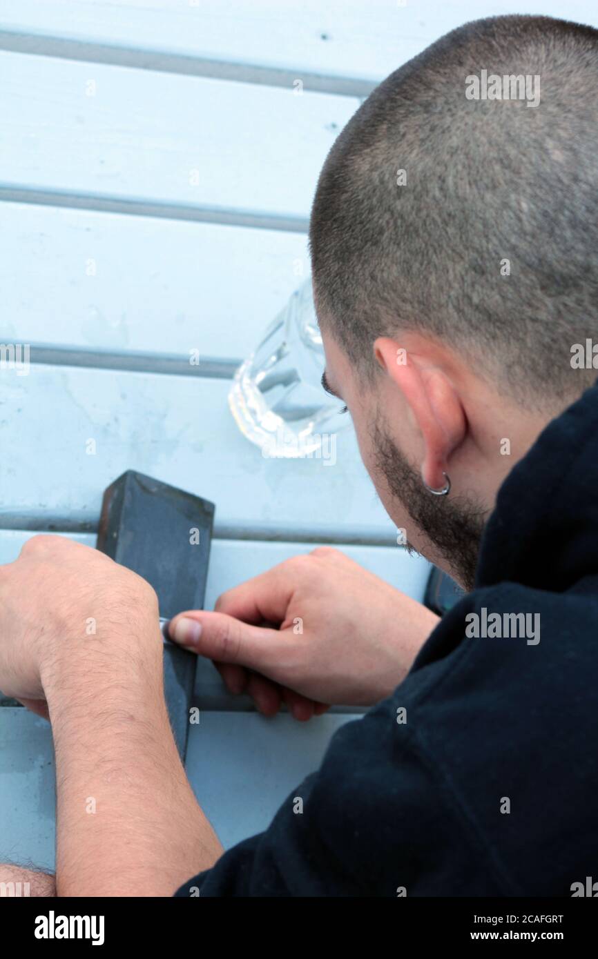 Primo piano di un giovane uomo che affila un coltello usando una pietra da ciminello Foto Stock