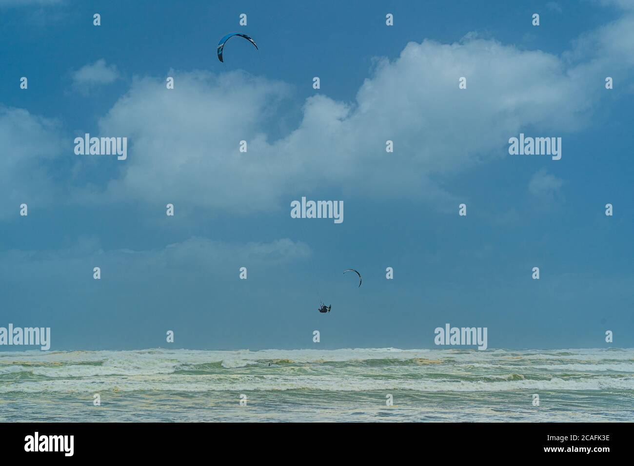 Un kitesurfer salta nell'aria sopra le grandi onde tempestose a Muriwai Beach, Auckland, Nuova Zelanda. Foto Stock