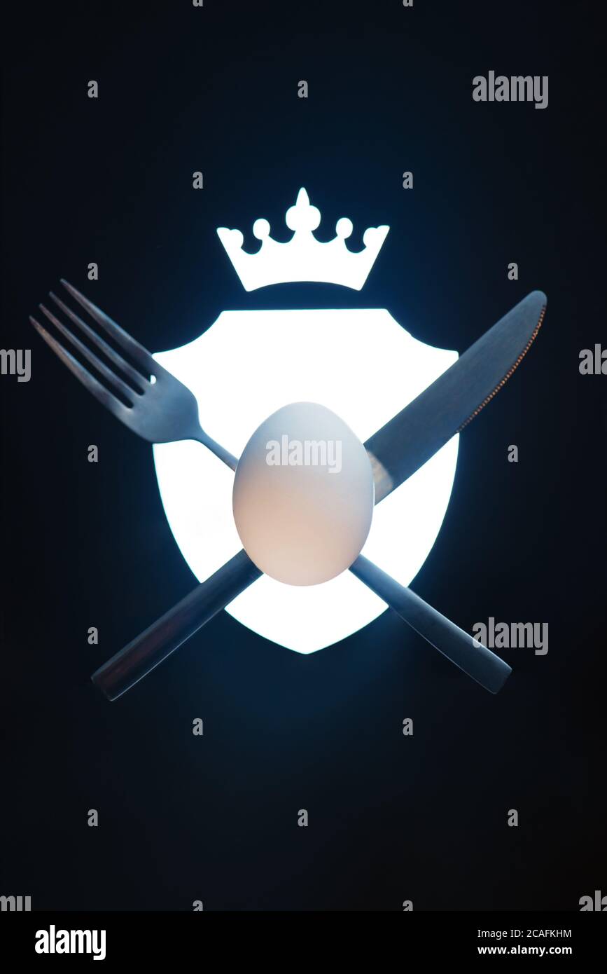 Stemma con forchetta, coltello e un uovo, simbolo del cibo, fotografia alimentare creativa Foto Stock