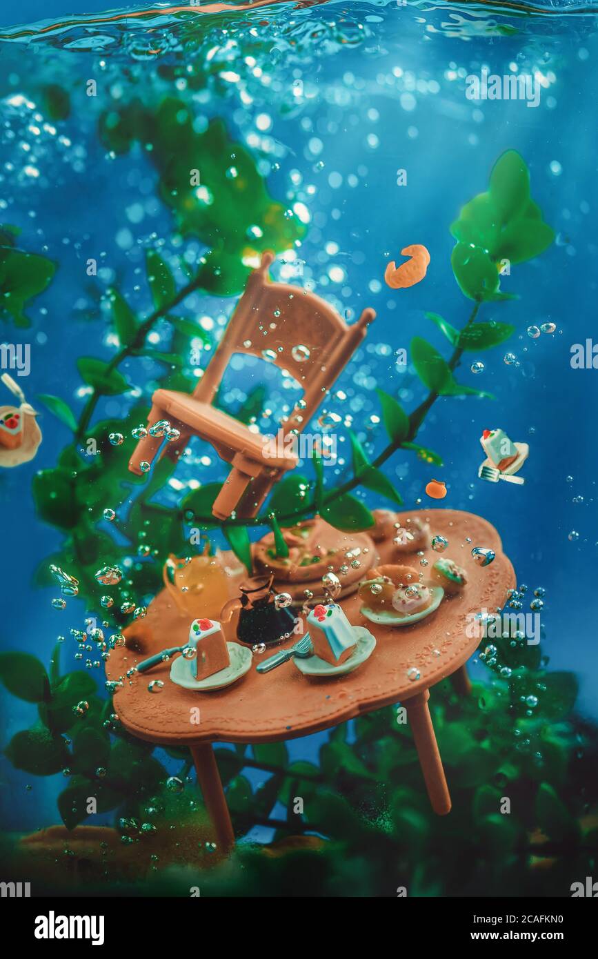 Festa del tè sott'acqua, tavolo affogante con dolci e una sedia, alghe e bolle, vita morta sott'acqua Foto Stock