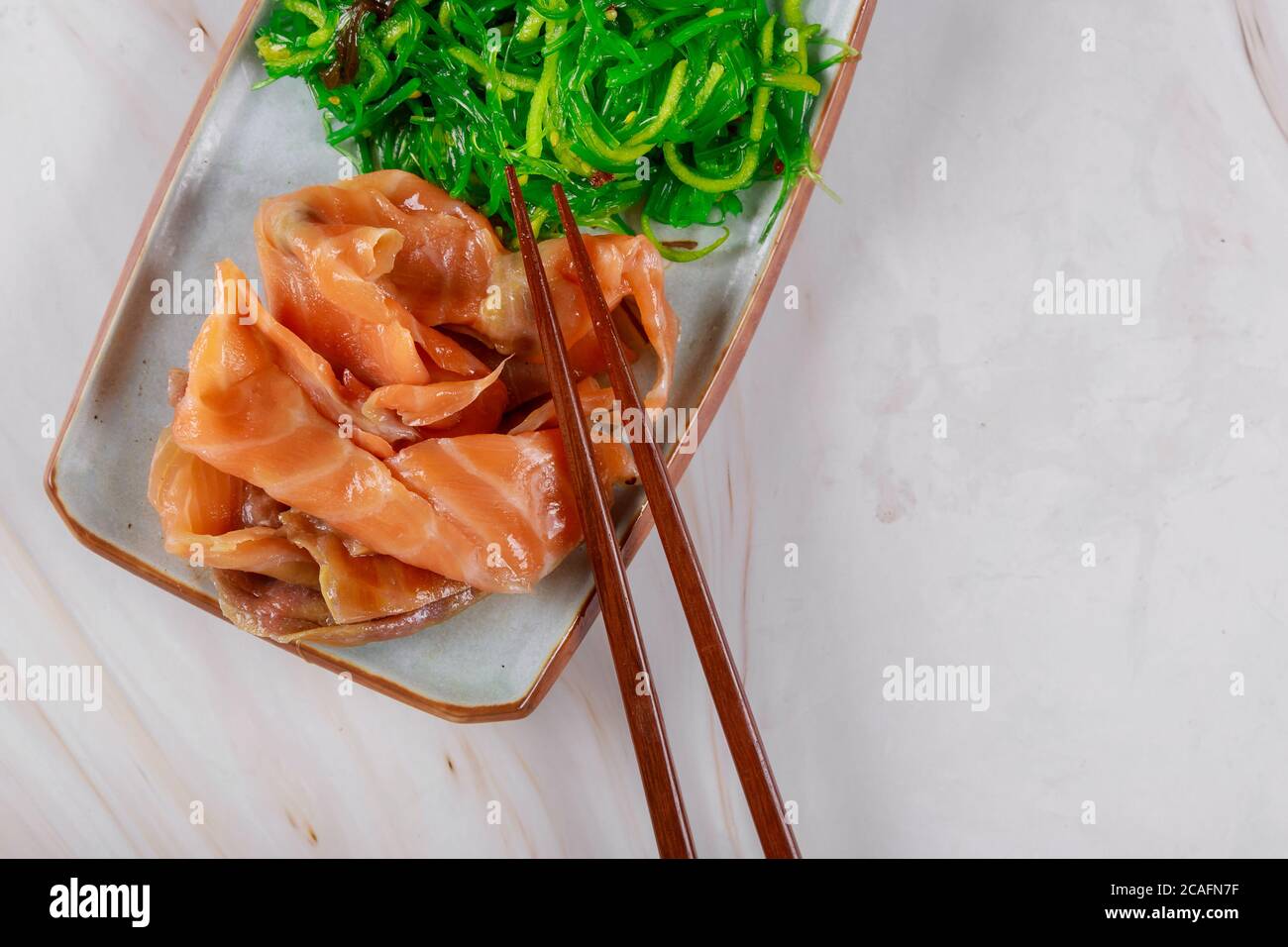 Il piatto coreano affetta il salmone con insalata di alghe e bastone di legno Foto Stock