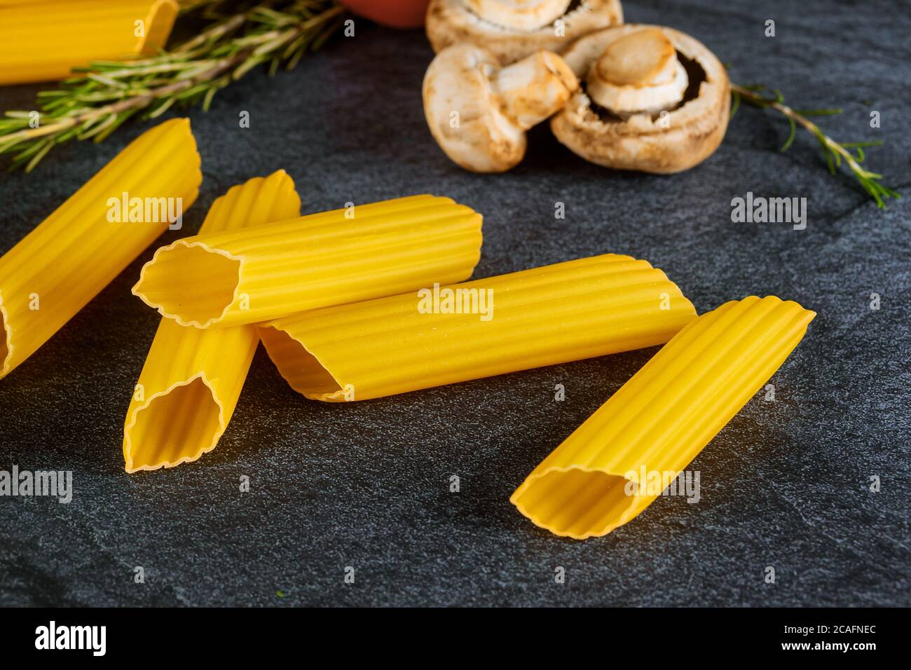 Cannelloni pasta secca con funghi e pomodori su fondo nero. Cucina italiana. Foto Stock