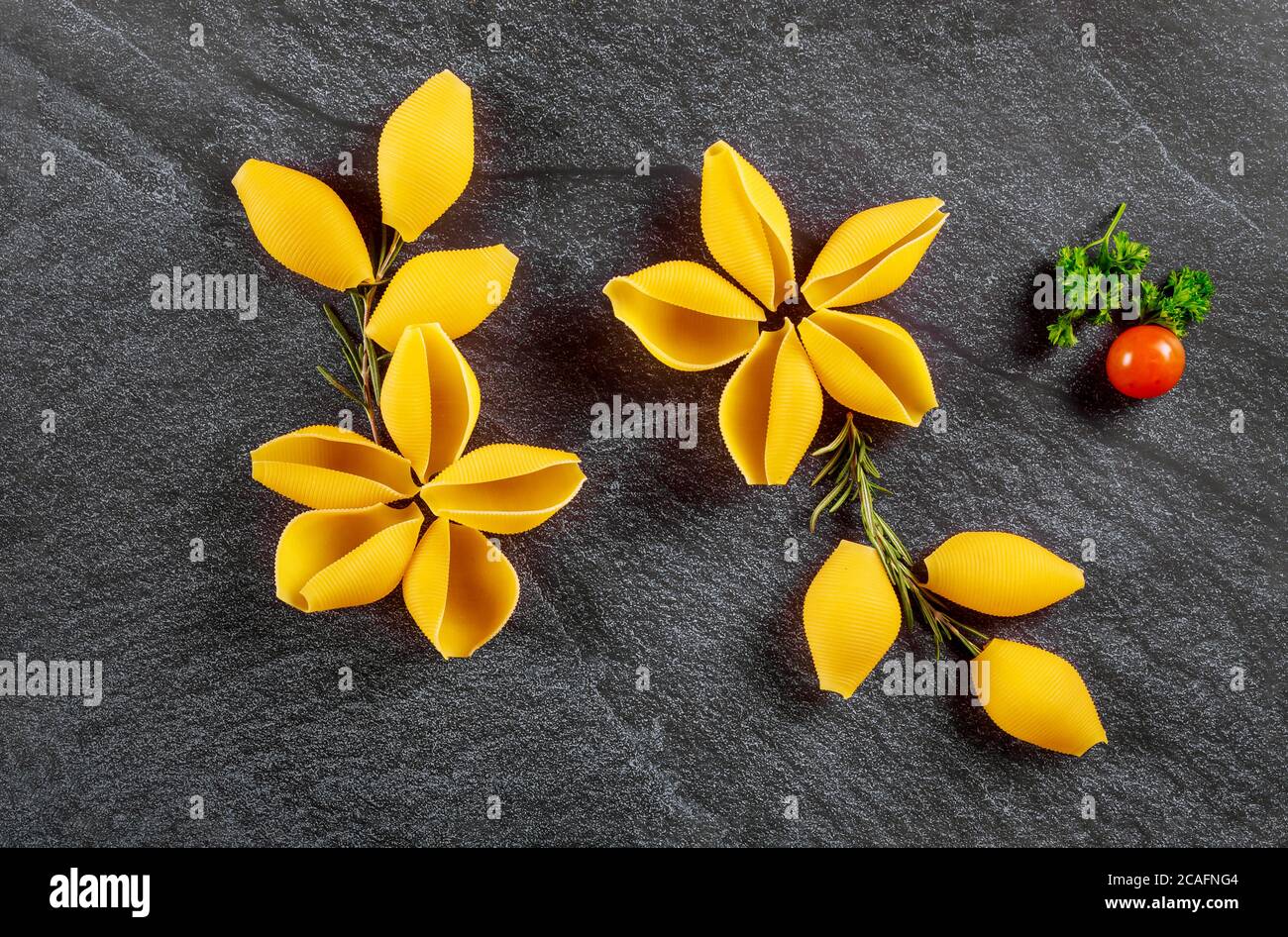 Conchiglie asciutte come un fiore con pomodoro su nero sfondo di pietra Foto Stock