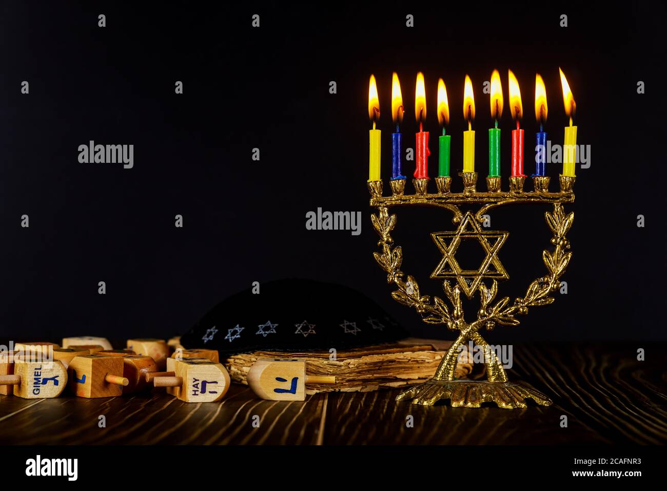 Menorah con candele a colori e Dreidel su sfondo nero. Foto Stock