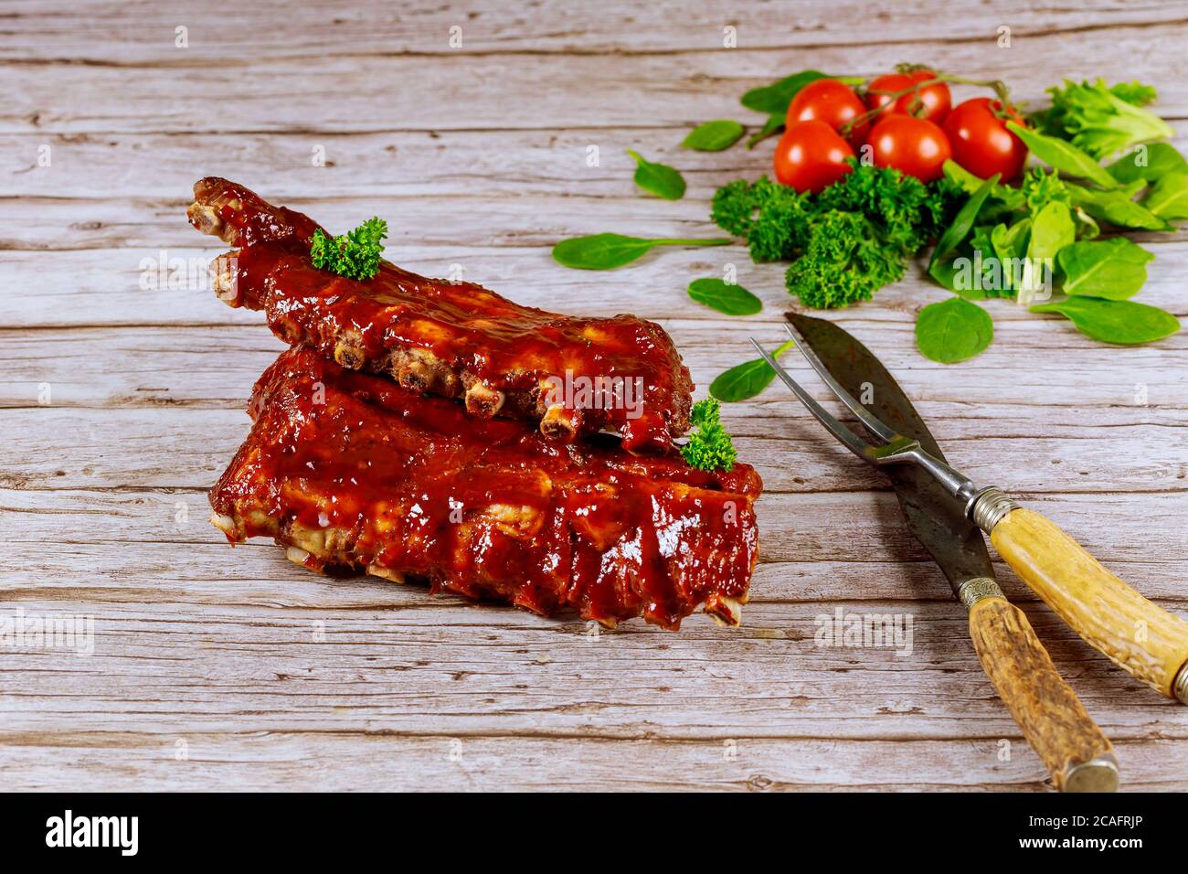 Costolette di maiale grigliate con salsa barbecue, pomodoro e spinaci su sfondo ligneo. Foto Stock