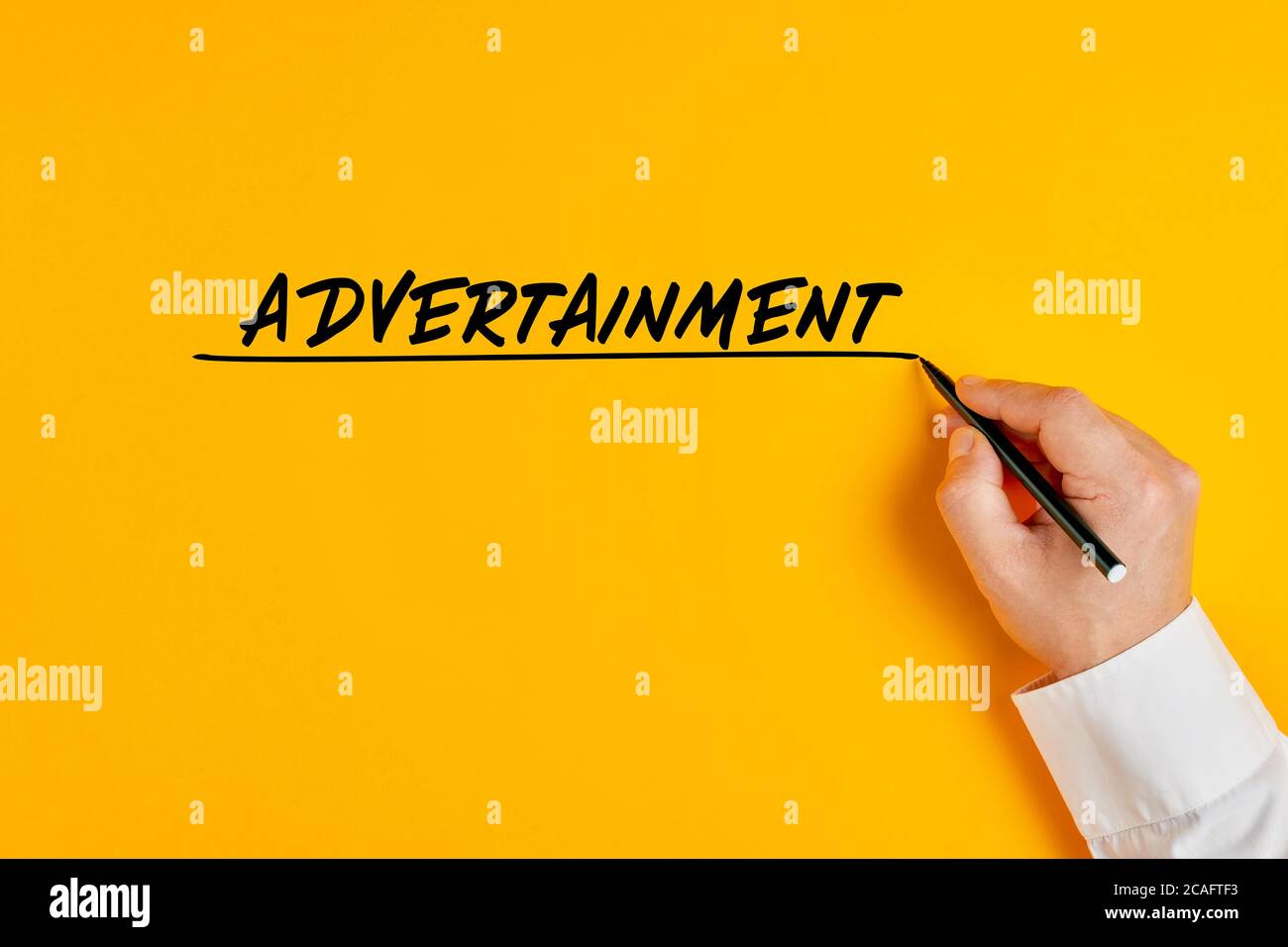 La mano maschile sta scrivendo la parola advertainment su sfondo giallo. Concetto di buzzword di affari che intagrates la pubblicità e l'intrattenimento. Foto Stock