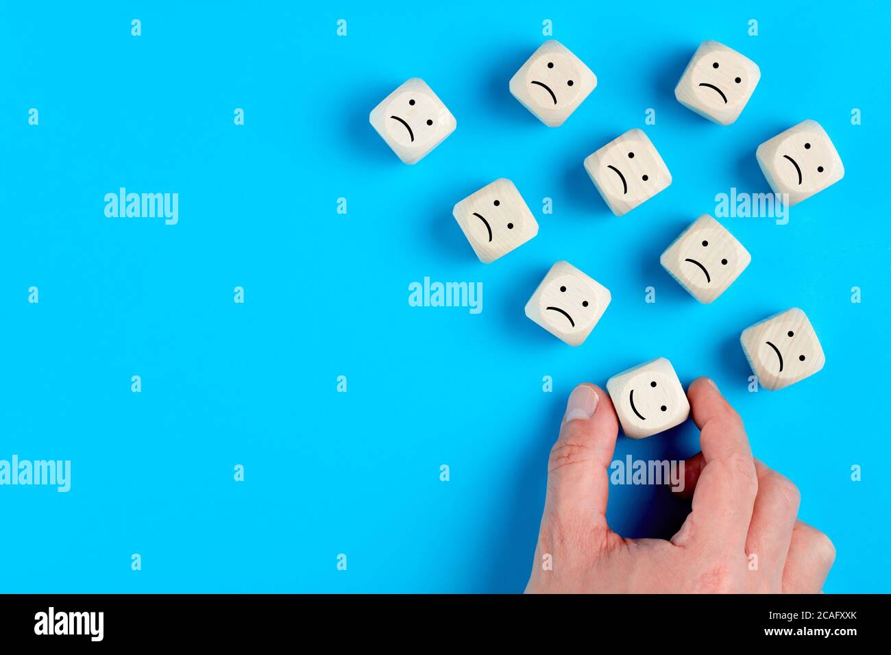La mano maschile sceglie il volto felice tra i volti infelici su blocchi di legno. Concetto di soddisfazione del cliente o feedback positivo. Foto Stock