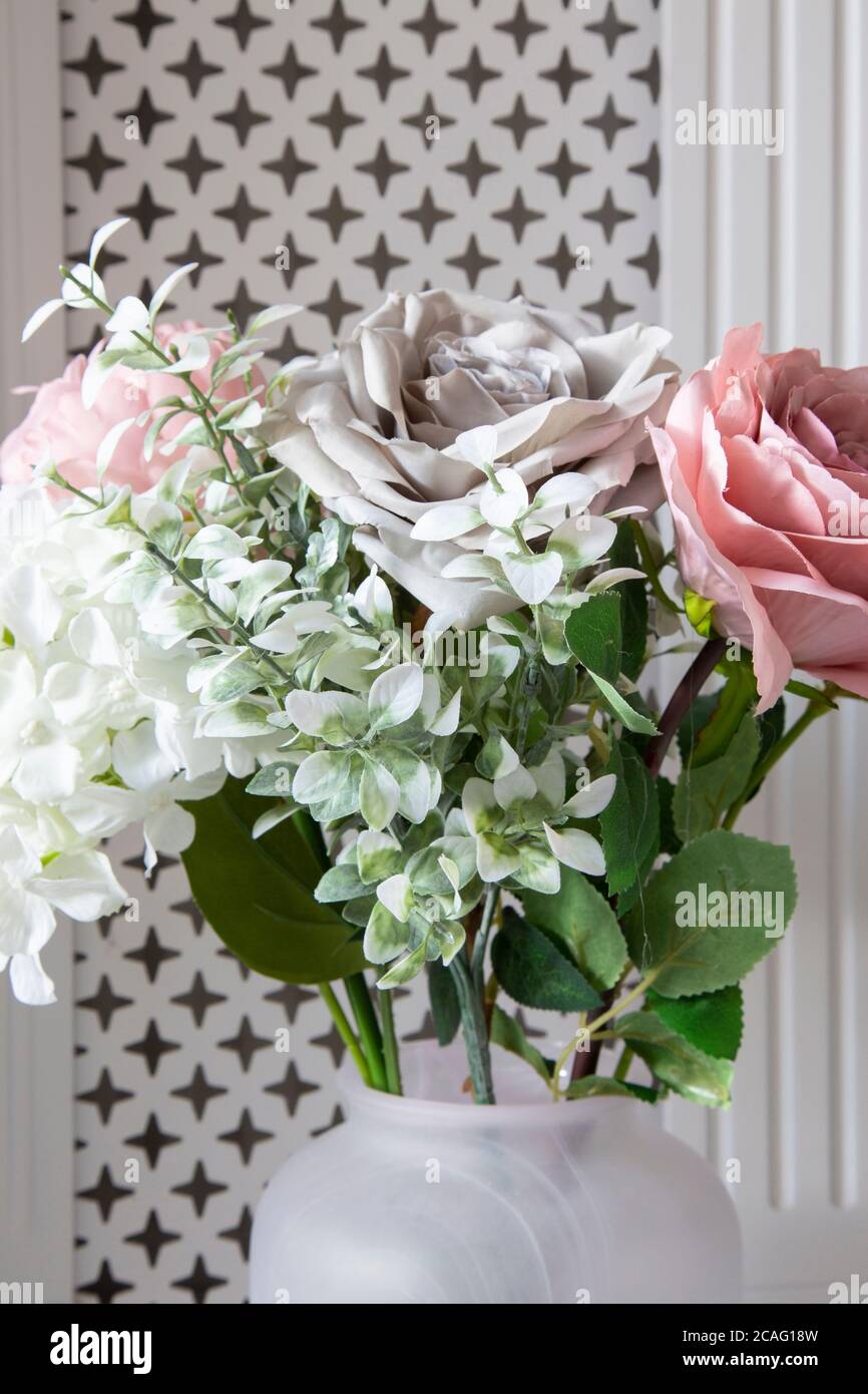 Bouquet di fiori artificiali in un vaso di fronte un coperchio bianco del radiatore Foto Stock