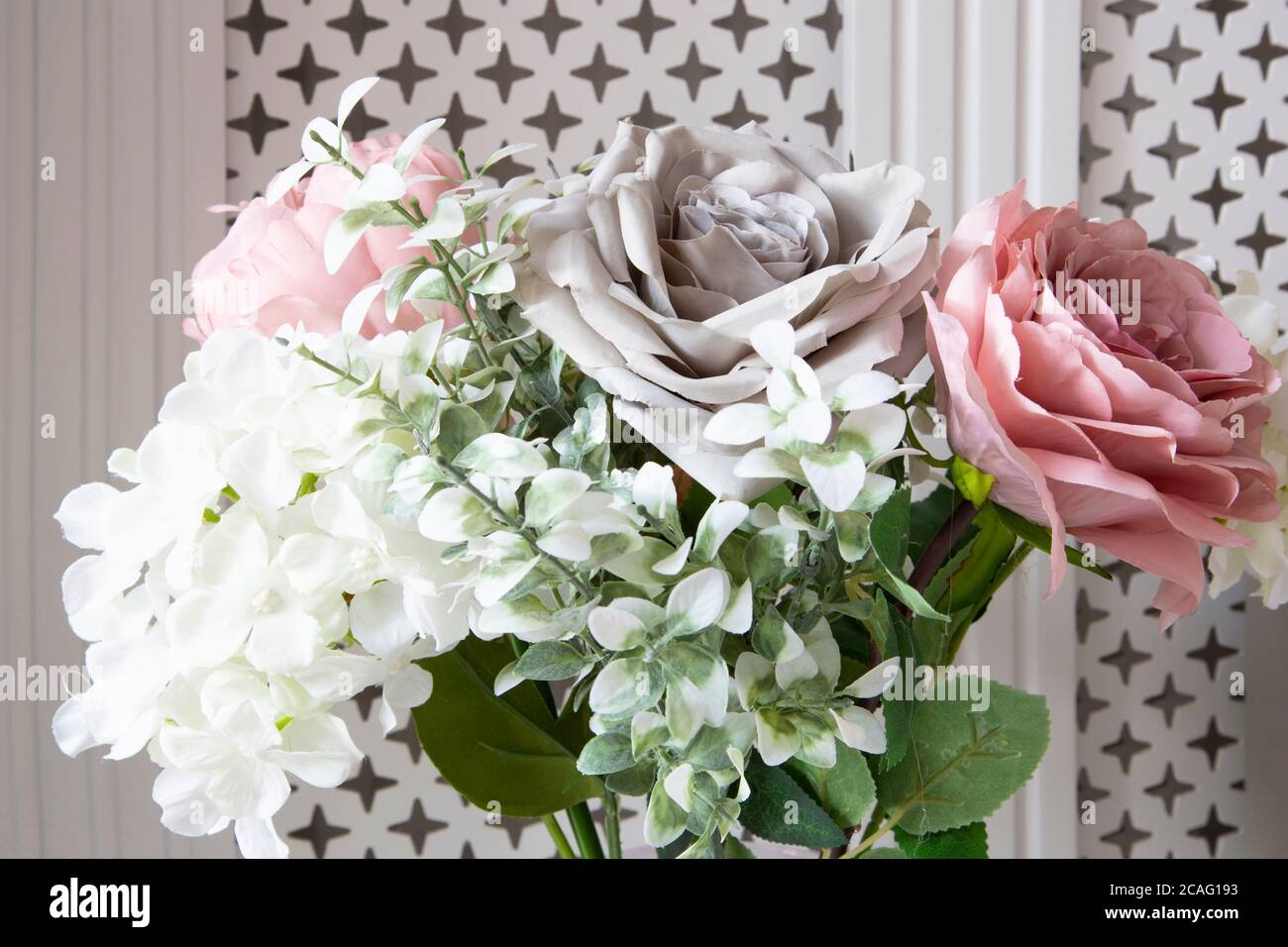 Bouquet di fiori artificiali in un vaso di fronte un coperchio bianco del radiatore Foto Stock