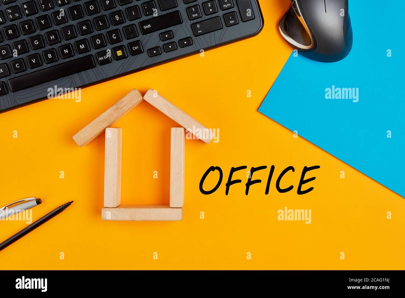 Home Office o il concetto di lavoro da casa. Spazio di lavoro superiore con icona casa fatta con blocchi di legno e scritta a mano parola ufficio su sfondo giallo. Foto Stock