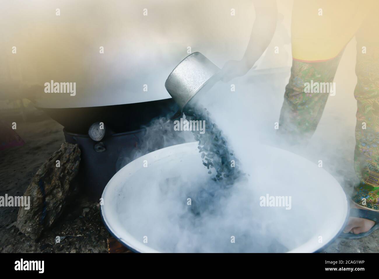 Una donna asiatica arrostire i chicchi di caffè in modo tradizionale. Mettere a fuoco la paletta argentata. Foto Stock