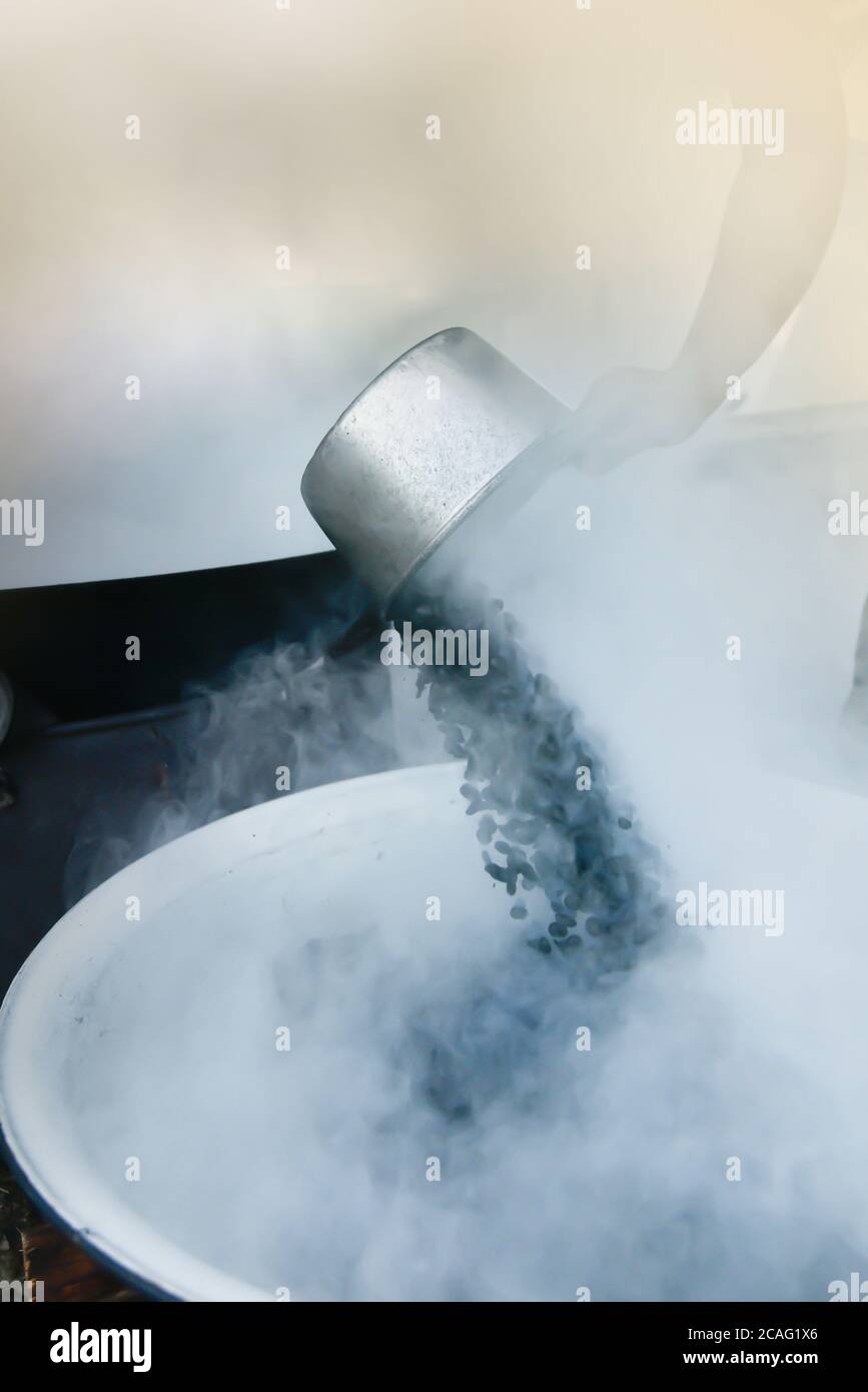 Una donna asiatica arrostire i chicchi di caffè in modo tradizionale. Mettere a fuoco la paletta argentata. Foto Stock