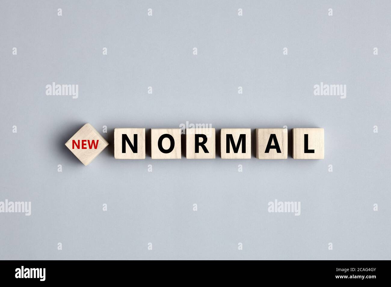 La parola nuova normalità durante i giorni della pandemia del coronavirus è scritta su cubi di legno su sfondo grigio. Foto Stock